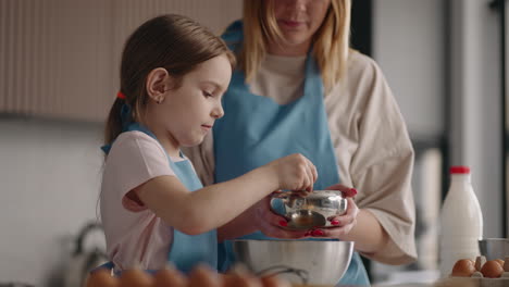 Una-Niña-Linda-Y-Curiosa-Está-Ayudando-A-Su-Madre-En-La-Cocina-Vertiendo-Azúcar-En-Un-Tazón-Infancia-Feliz